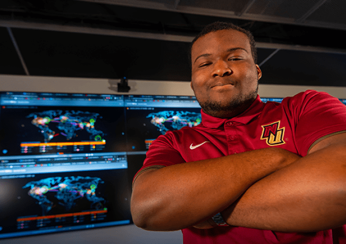 Student standing in front of large cyber screens inside the war room.